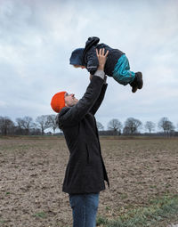 Side view of playful father lifting daughter on field during winter