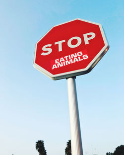 Low angle view of road sign against clear blue sky