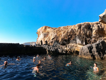 People swimming in sea against clear blue sky