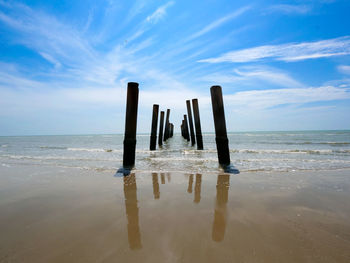 Wooden posts in sea against sky