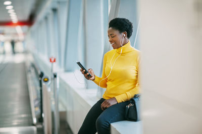 Attractive african girl is waiting for a train in the subway and listening to music with headphones.