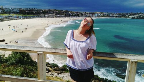 Portrait of young woman standing by railing against beach