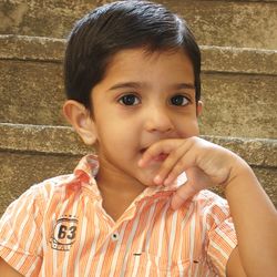 Close-up portrait of cute boy with finger in mouth against wall