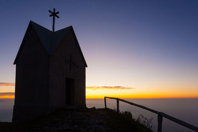 Silhouette building by sea against sky during sunset