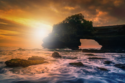 Rock formation in sea against sky during sunset