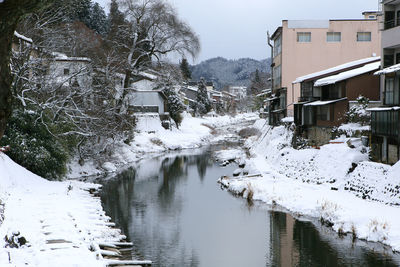 Snow covered houses by canal amidst buildings during winter