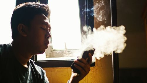 Close-up of man smoking while holding mobile phone at home