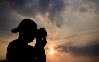 Silhouette woman photographing against sky during sunset