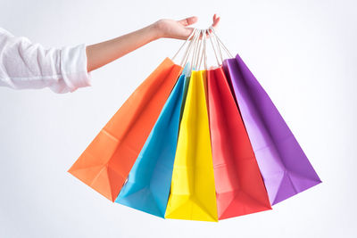 Cropped hand of woman holding shopping bags against white background