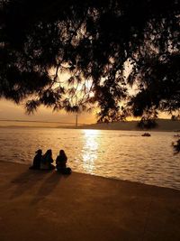 Silhouette people looking at sea during sunset