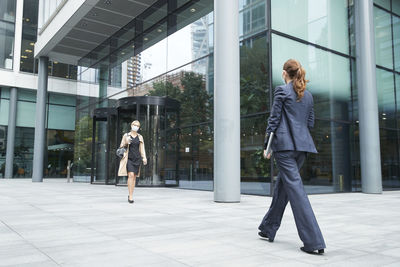 Business people wearing face mask while walking against office building