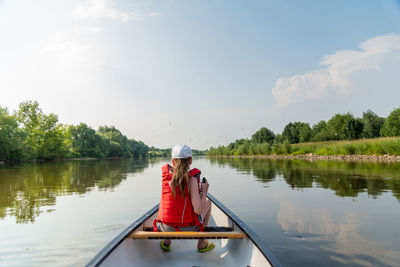 Rear view of people sitting on boat in lake against sky