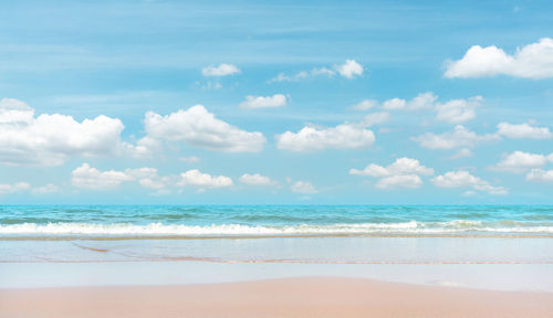 Brown sand beach on blue sea water and white wave under white clouds and pastel blue sky background