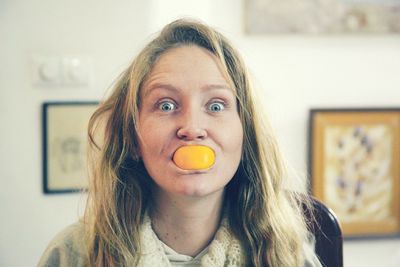 Portrait of young woman carrying orange in mouth