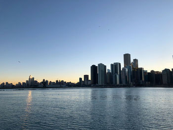 Sea by buildings against clear sky during sunset