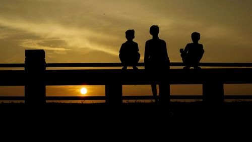 Silhouette male friends on railing against orange sky