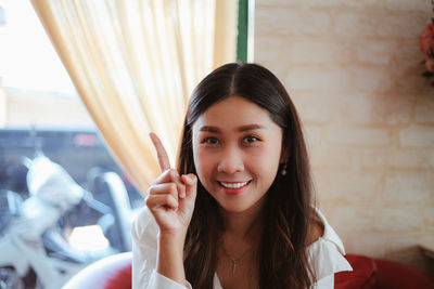 Portrait of smiling woman gesturing while sitting at home