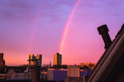 Rainbow over city against sky at sunset