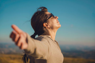 Side view of happy mid adult woman with arms outstretched standing on mountain against blue sky