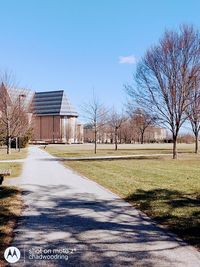 Road amidst bare trees and buildings against clear blue sky