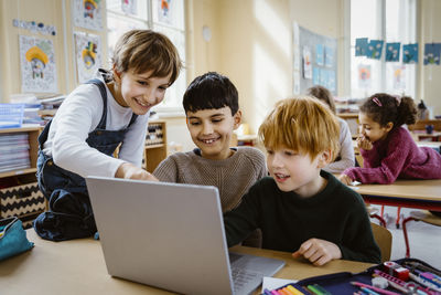 Happy schoolboys using laptop together at desk in classroom