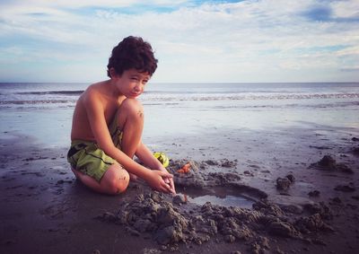 Boy playing with sand at beach against sky
