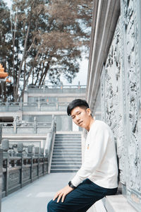 Side view portrait of young man sitting against wall in city