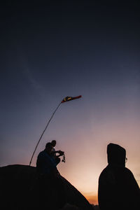 Silhouette man holding bird flying against sky during sunset