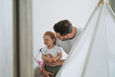 Father young man and crying upset baby girl little daughter in children room at home