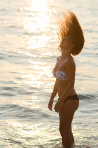 Sensuous woman in bikini tossing hair while standing in sea