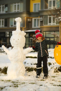 Winter portrait of children with a plastic sled sliding on a snowy slope and making a snowman