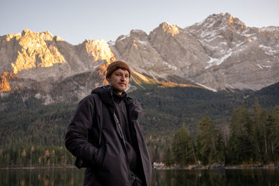 Portrait of young man sanding by lake against mountain range