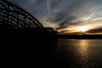 Silhouette bridge over river against sky during sunset