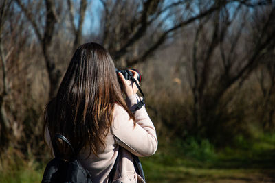 Beautiful woman taking a picture of a dry trees forest back shot closeup person