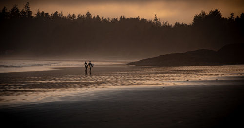 Silhouette people on beach against sky during sunset