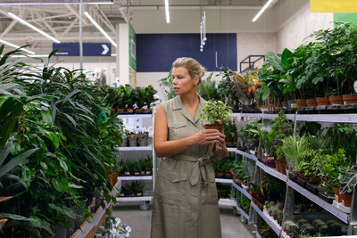 Woman at shopping, young lady choosing home plants in store