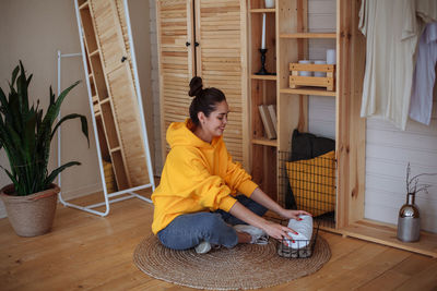 Woman at home sits on the floor on a wardrobe trunk near the closet and puts towels in the basket