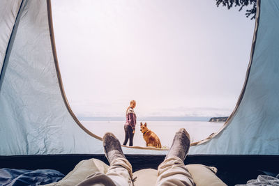 Low section of man with woman and dog in background against sky