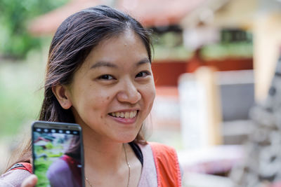 Portrait of smiling young woman showing mobile phone