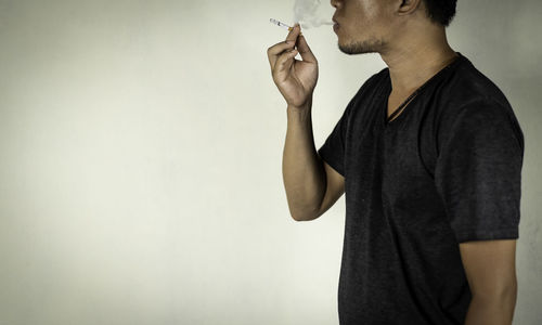 Midsection of man holding cigarette against wall
