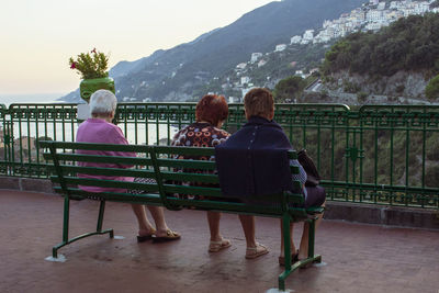 Rear view of people sitting on bench looking at mountain