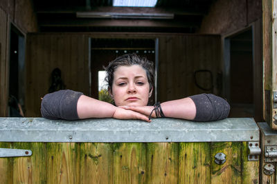 Portrait of woman leaning on wooden gate in stable