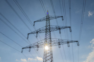 High voltage power line backlit against blue sky