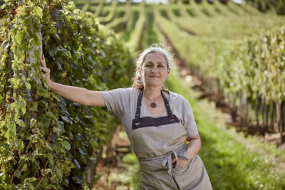 Smiling farmer with hand in pocket by grape vine at vineyard