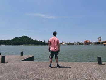 Rear view of man looking at lake against sky