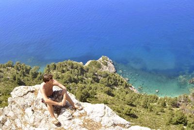 Woman sitting on rock looking at sea