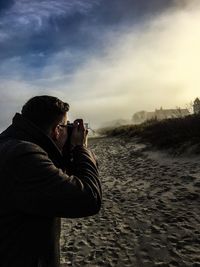 Rear view of woman photographing through smart phone during winter