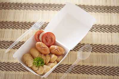 High angle view of sausages with vegetable slices in container on table