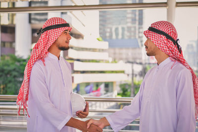 Side view of smiling businessman shaking hands with colleague on elevated road in city