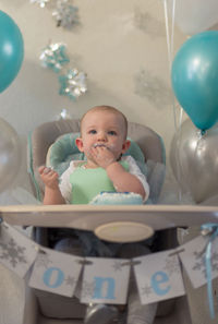 Cute baby boy eating cake while sitting on chair at home